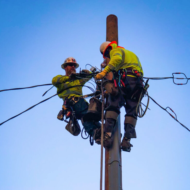 Two Harlan Electric workers on the pole of a power line