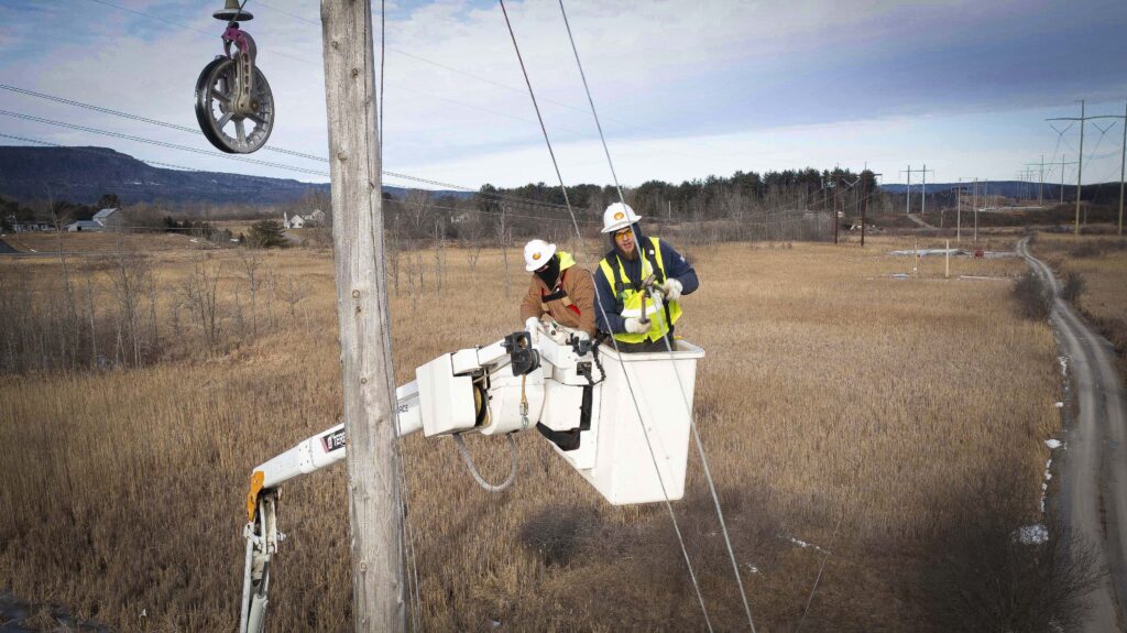 Two lineworkers work on power lines from a bucket truck.