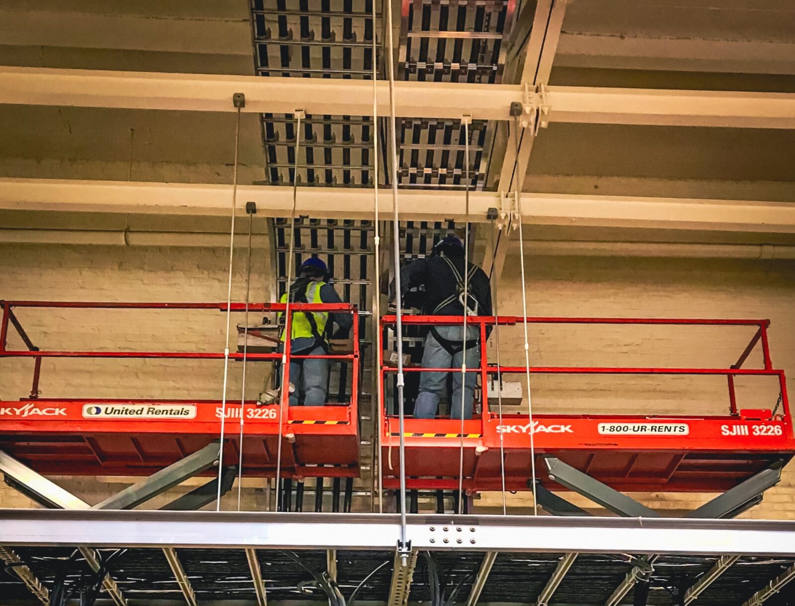 Two workers using skyjacks to reach ceiling pipes